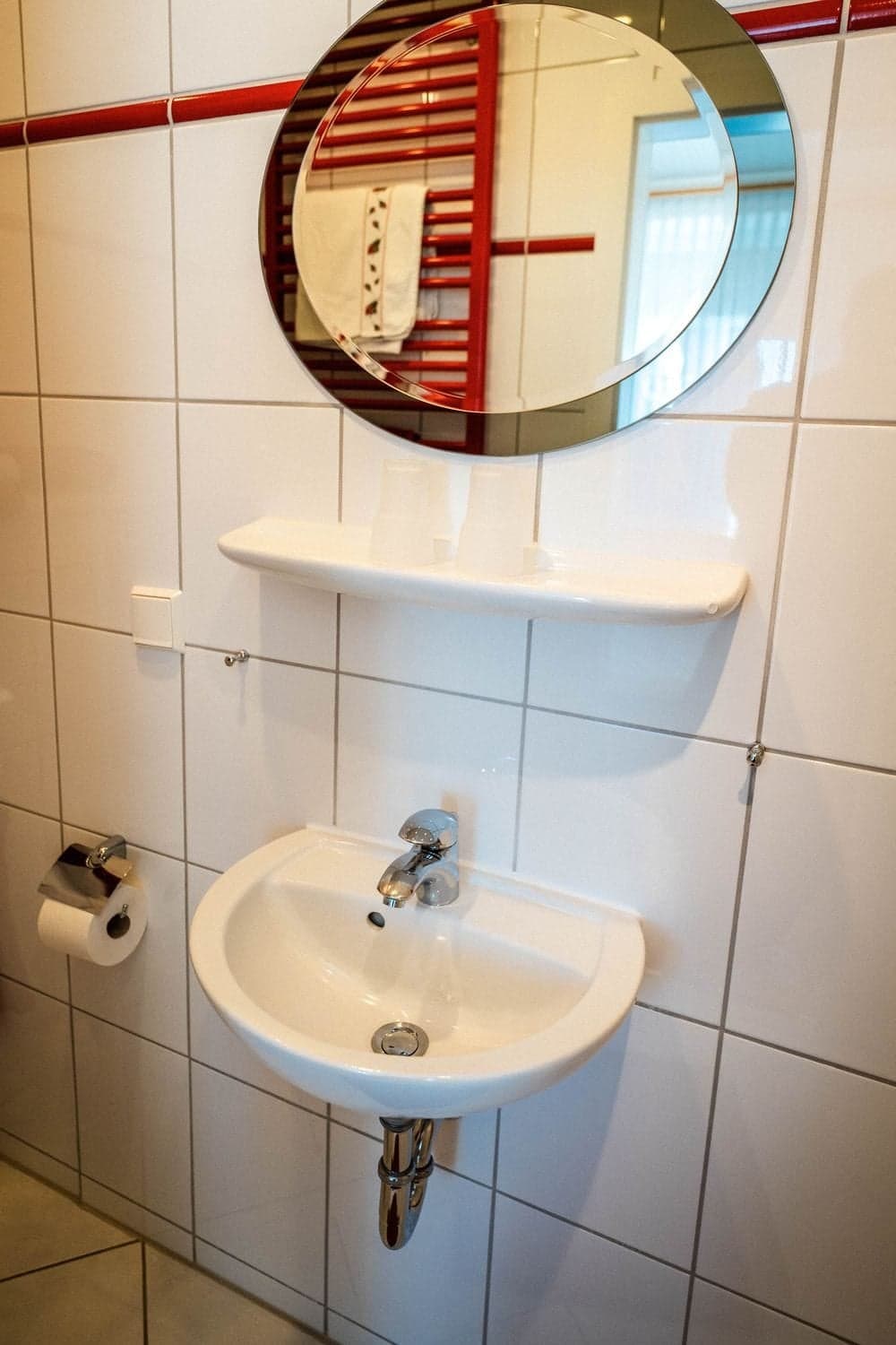 Waschbecken mit rundem Spiegel und Ablage in einem weiß gefliesten Bad
